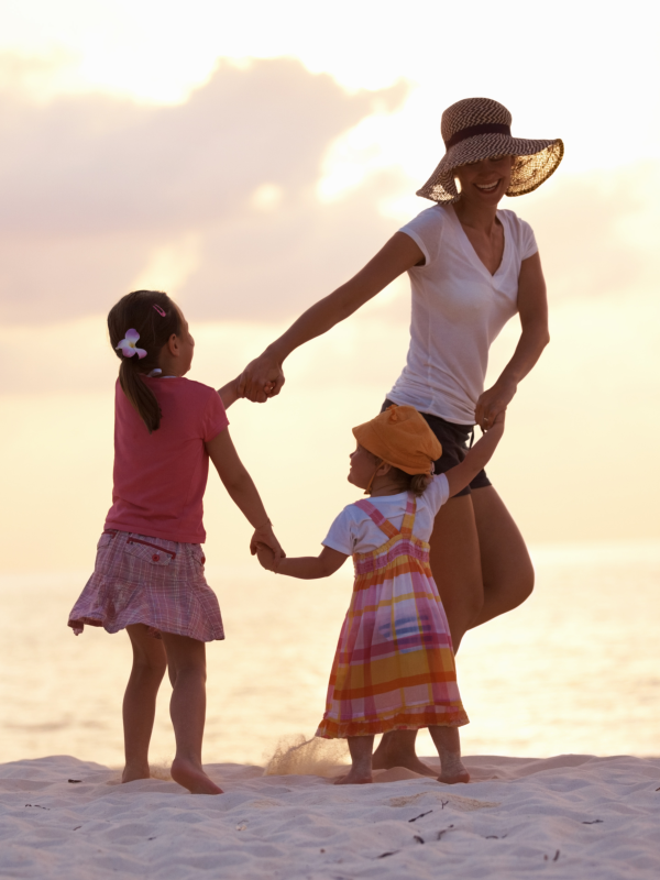 Happy relaxed mother holding hands with her two daughters at the beach, sunset.